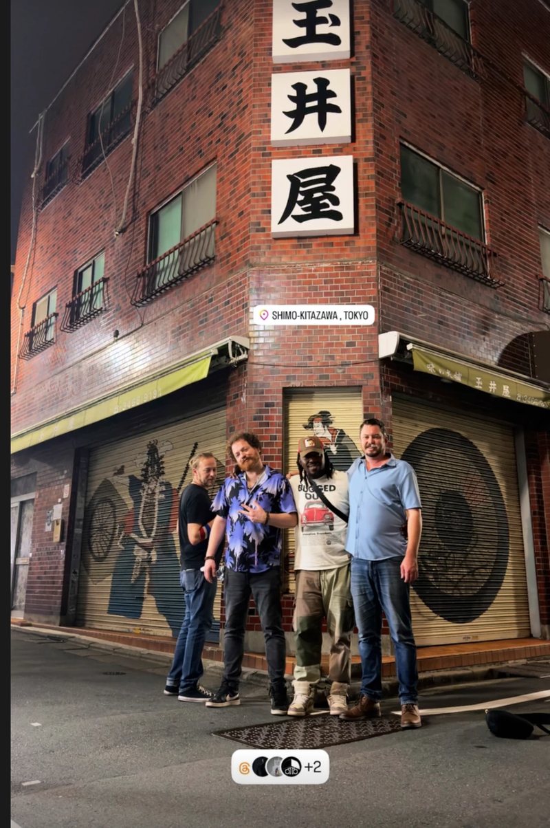 Dave Menzo and the band on a street corner in Shimokitazawa at night, under a 玉井屋 sign
