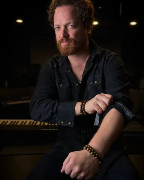 Dave Menzo seated in a recording studio, sleeves rolled